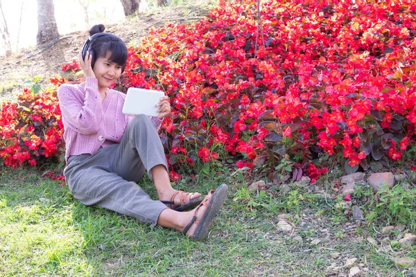 Mulher Usando Fones Ouvido Usar Celular Fundo Parque Flores Vermelhas — Fotografia de Stock