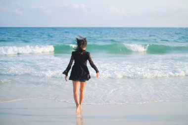 Sahildeki kumlu sahilde bulanık mavi denizle yürüyen bir kadın. Turistler tatil konseptinde tropikal yaz tatiline giderler. Otantik ten rengi, ince yapılı ve siyah saçlı Asyalı bayan. Okyanus Koh Samet Adası Rayong Tayland