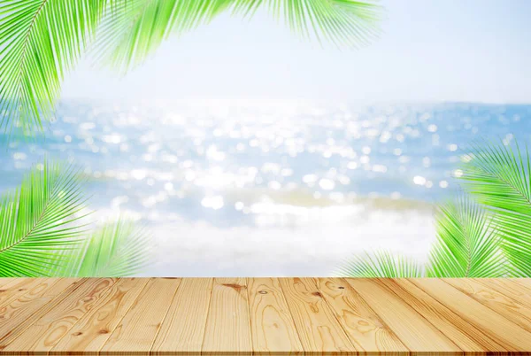 Denizde, arka planda palmiye yaprakları olan bir masa. Bulanık mavi okyanus kumunun üzerinde ahşap ve sahilde parlak bir kırbaç. Bulanık su üzerinde model tezgah bar montajı. Turizm seyahati tropikal yaz tatili.