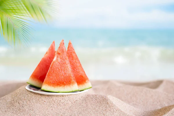 Watermelon in plate on sand beach at coast of seaside and blue sky background.tropical fresh snack fruits for tropical tourist travel summer holidays. fresh orgarnic sweet and red fruits.food for diet