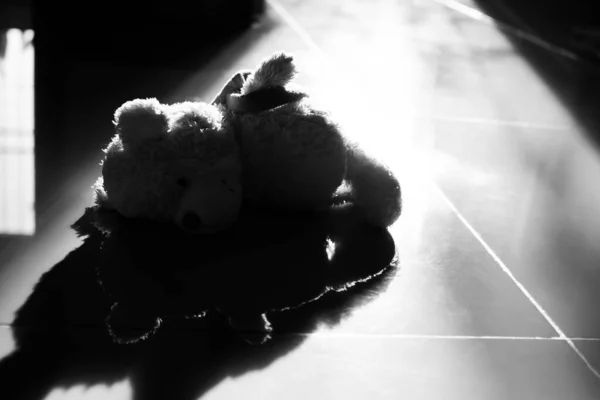 Alone teddy bear sleep on floor with overlight. black and white. cute toy doll in room with free  space. card or poster for lonely, sad, broken heart or international missing children\'s day concept.