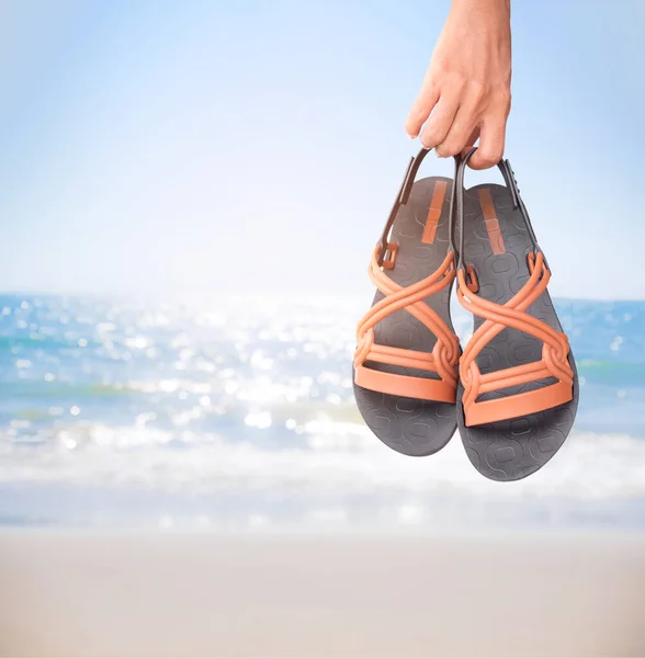 Close up woman holding flip flop on blur sand beach,blue sea and blue sky seascape background. empty free space Panorama for presentation island ocean water nature. tourist tropical summer holidays.