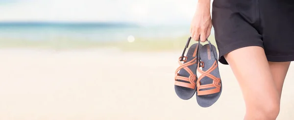 Close up woman holding flip flop on blur sand beach,blue sea and blue sky seascape background. empty free space Panorama for presentation island ocean water nature. tourist tropical summer holidays.