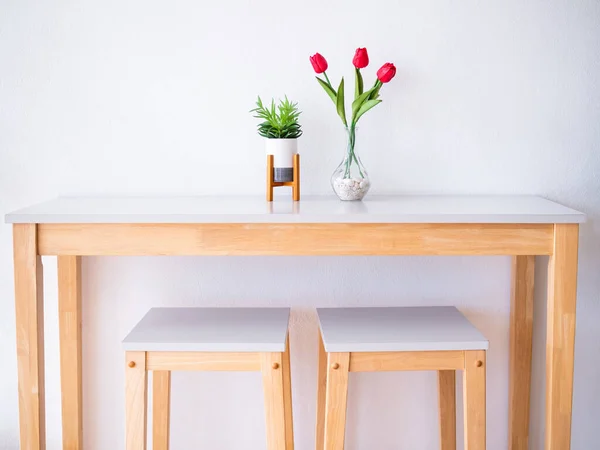 Wooden Table and chair with flowers tulips in vase on table and white wall background.interior modern painting design dinning in small kitchen room at apartment or home.scandinavian furniture design.