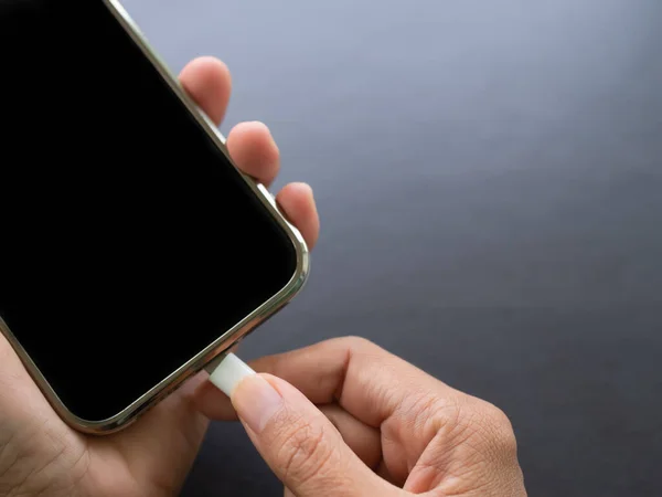 Finger plugging a charger Mobile on Black wood background with free space.hand woman holding cable mobile charger to connect smartphone. Technology for lifestyles or business finance concept.