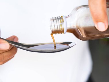 El ele tutuşan öksürük şurubu kaşığı yakın çekim, hastalık sorunu, hastane konsepti..