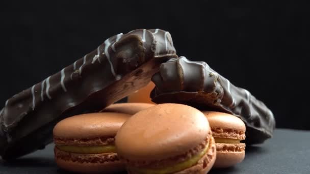 Chocolade en macaroon draaien op een zwarte achtergrond en de hand neemt snoep, snoepjes draaien — Stockvideo