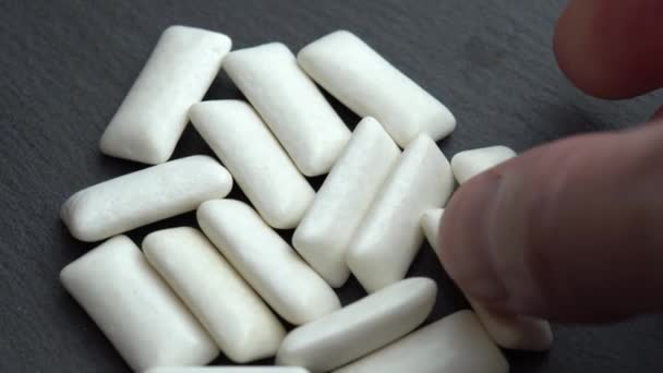 Bílé dragees z mátové žvýkačky otočit na černém pozadí a ruka má dvě podložky — Stock video