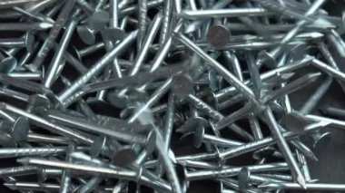 İnşaat işleri için metal çiviler dönen siyah yüzeye saçılmış, çiviler yakın arkaplanda dönüyor, inşaat işleri için çivi ya da çivi çakılıyor