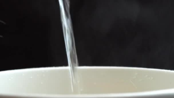 Dodawanie wrzącej ciepłej wody do makaronu instant z rozpryskami, opakowanie makaronu obracają się na czarnym tle, azjatyckie słodkie i kwaśne makaron — Wideo stockowe