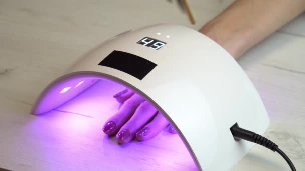 Flicka placerade handen under en nagellampa och väntar på att nagellacket ska hårdna, ultraviolett nagellampa — Stockvideo
