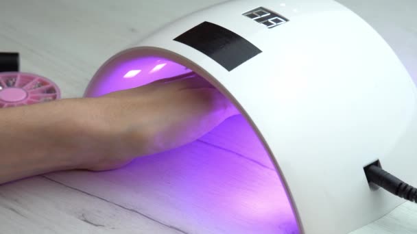 女の子は爪ポーランド硬化ランプの下に手を置き、爪の研磨が硬化するのを待ちます,紫外線ネイルランプ — ストック動画