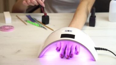 Kız elini ojenin altına koyup ojenin sertleşmesini bekliyor. Ultraviyole oje lambası.