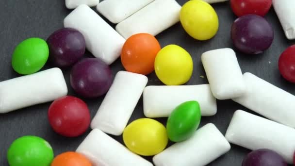 Sweets colored candies skittles and mint chewing pads, colored sweets rotate on a black plate — Stock Video