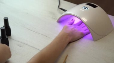 Kız elini ojenin altına koyup ojenin sertleşmesini bekliyor. Ultraviyole oje lambası.