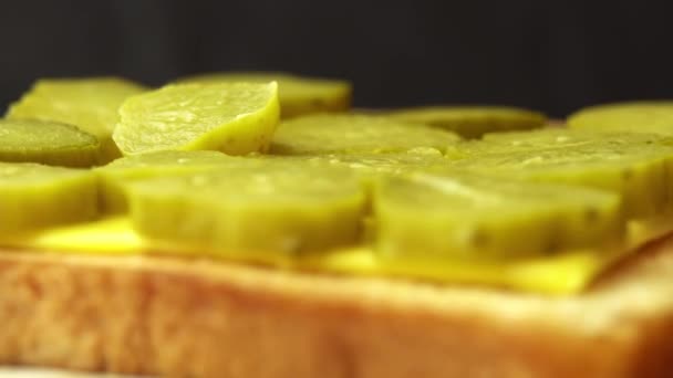 Sandwich tostado con queso y pepino en vinagre gira sobre un fondo negro — Vídeo de stock