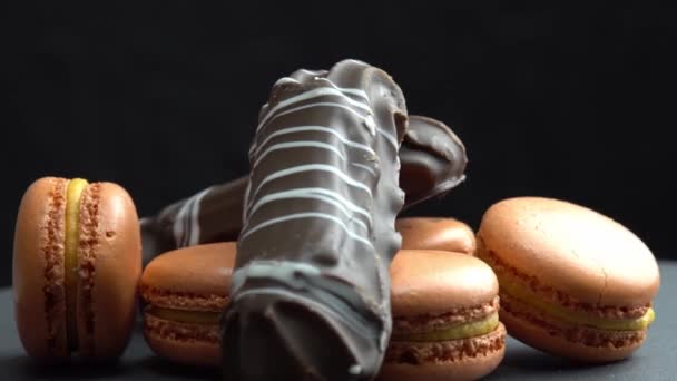 Chocolate y macarrón giran sobre un fondo negro, sabrosos dulces, dulces giran macro — Vídeo de stock