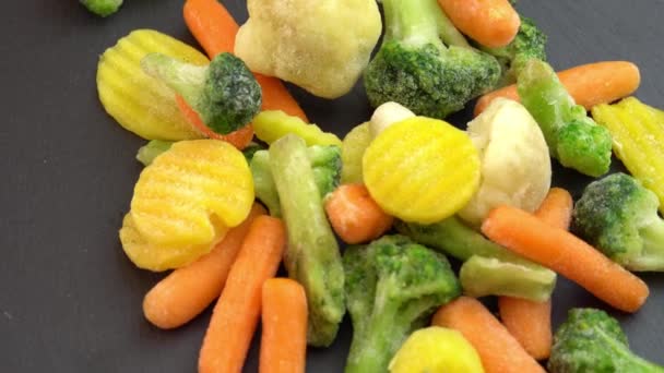 Здоровое питание или диетическая пища для вегетарианцев и веганов, свежие замороженные овощи, вращающиеся на черном фоне, замороженная цветная капуста, брокколи и детская морковь — стоковое видео