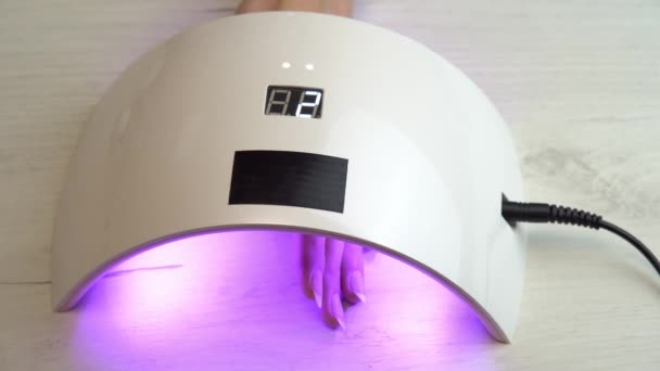 Lány helyezett kéz alatt egy körömlakk gyógyító lámpa, és várja a körömlakk megkeményedik, ultraibolya körömlámpa — Stock videók