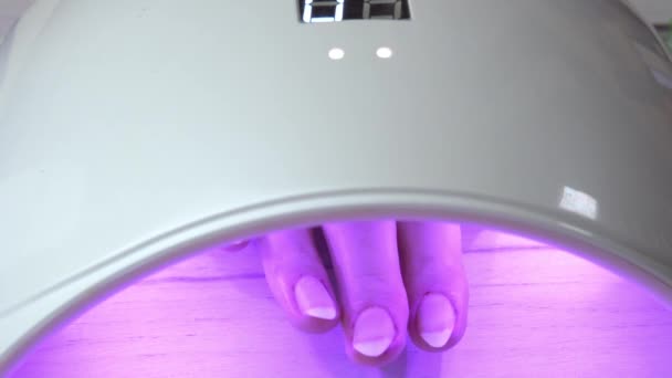 Fille placée la main sous une lampe à ongles et attend que le vernis à ongles durcisse, lampe à ongles ultraviolette — Video