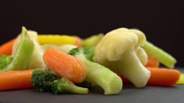 Färska frysta grönsaker roterande på svart bakgrund, hälsosam mat eller kost för vegetarianer och veganer, frysta blomkål, broccoli och morötter baby — Stockvideo