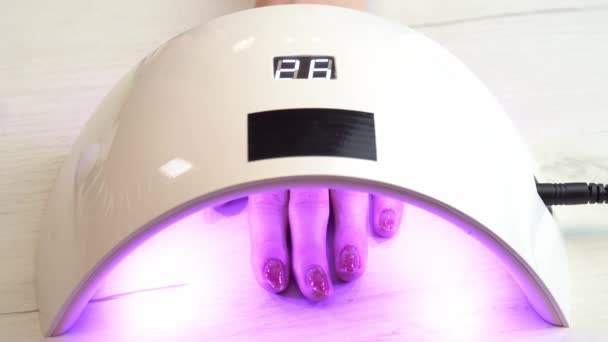 Flicka placerade handen under en nagellampa och väntar på att nagellacket ska hårdna, ultraviolett nagellampa — Stockvideo