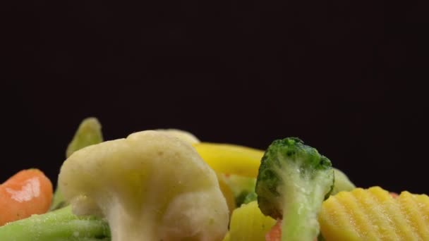 Verduras frescas congeladas girando sobre fondo negro, alimentos saludables o alimentos dietéticos para vegetarianos y veganos, coliflor congelada, brócoli y zanahorias bebé — Vídeo de stock