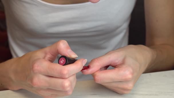 Κορίτσι κάνει στον εαυτό της ένα μανικιούρ και βάφει τα νύχια της με κόκκινο βερνίκι νυχιών με λάμψη — Αρχείο Βίντεο