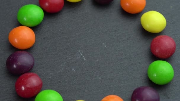 Colored candies rotate on a black background and the hand takes one candy, colored sweets — Stock Video