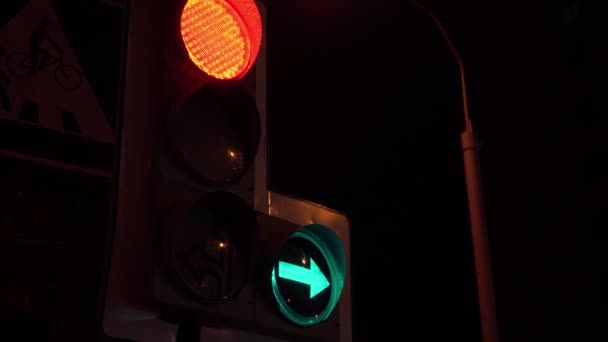 Feux de circulation avec feu rouge et flèche verte pointant vers la droite, coup de main. Gros plan des feux de circulation sur la route sur fond de ciel noir — Video