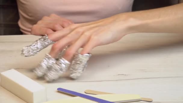 Het meisje bereidt haar nagels voor op nagellak verwijderen door ze in folie te wikkelen en heeft plezier tijdens het wachten. Voorbereiden op een manicure — Stockvideo