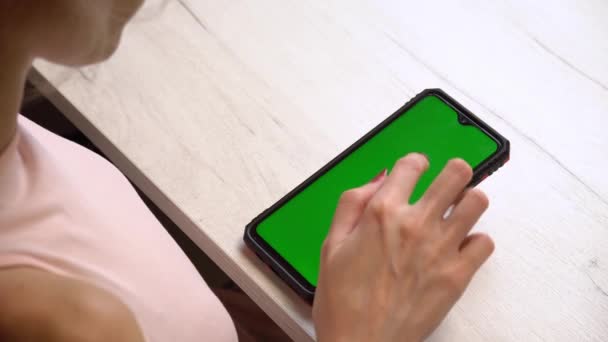 Een meisje gebruikt tijdens een manicure een smartphone met een groen scherm. Zelfgemaakte manicure service. Manicure verft nagels met roze gellak. Gemanicuurde rode nagels. Nagellak aanbrengen. — Stockvideo
