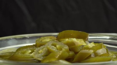 Dilimlenmiş jalapeno biberleri siyah arkaplanlı tabakta döner, yakın plan acı biber turşusu.