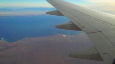 Uçak denizin ve çölün üzerinde uçuyor, uçağın kanadının penceresinden ve kanatlarından manzara.