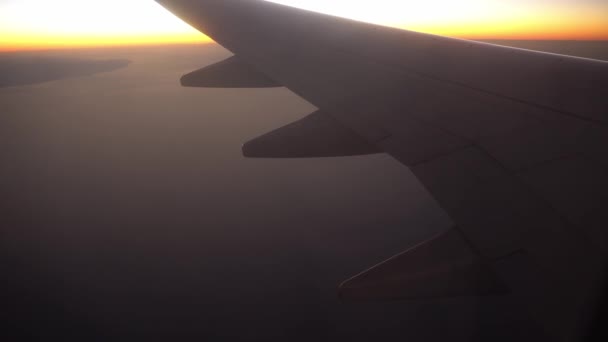 Flugzeug fliegt bei Sonnenuntergang oder Sonnenaufgang über das Meer und die Wüste, der Blick aus dem Fenster auf den Flügel des Flugzeugs und die Klappen. — Stockvideo