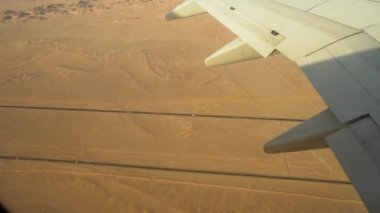 Uçak çölde otobanın üzerinden uçuyor, arabalar otoban boyunca gidiyor çöl manzarasında uçağın kanadının penceresinden