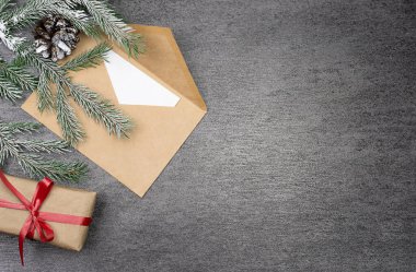Karda köknar dalı, bir külah, bir zarf ve bir hediye olan gri bir arkaplanda Noel kompozisyonu. Üst Manzara. Noel zamanı. Metin için bir yer var..