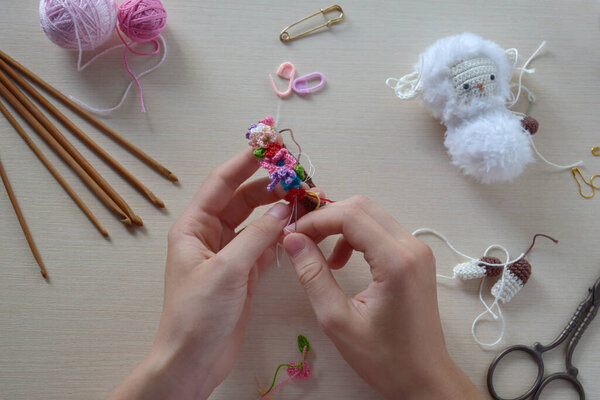 Делать попку из овец с венком из цветов. Вязаная овечка для ребенка. На столе нитки, иглы, крючок, хлопковая пряжа. Шаг 1 - вязать все детали игрушки. Ручные работы. Концепция DIY. Малый бизнес. Доход от хобби