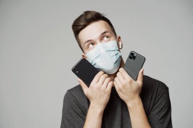 Genç bir adam iki telefon tutar, seçmeden önce düşünür. portre o