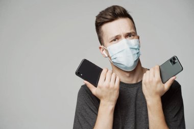 Genç bir adam iki telefon tutar, seçmeden önce düşünür. portre o