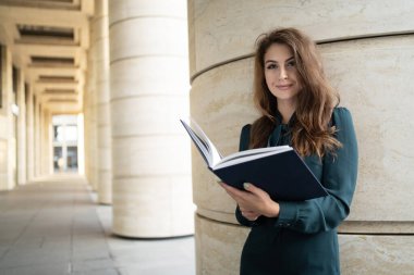 Öğretmen, elinde bir dizüstü bilgisayar ve çalışan bir ofis klasörü var. 
