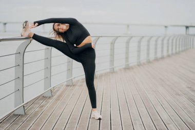 Genç kız bacak esnetme egzersizleri yapıyor. siyah eşofman. iyi