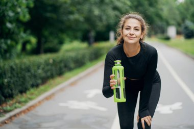 Kameraya su şişesiyle poz vermek. Sportif esmer kadın.