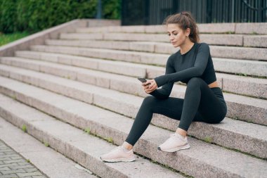 Basamaklarda oturmak, telefonda bir arkadaşla mesajlaşmak,