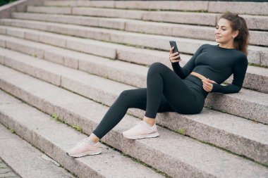 Ailesiyle mesajlaşıp, elinde telefonla oturuyor. Evet.