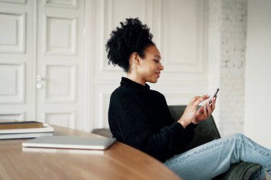 Brezilya görünümlü bir kız öğrenci elinde bir telefon tutuyor.