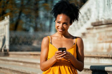 Telefonunda internette geziniyor. Mola sırasında dizüstü bilgisayara bir mesaj yazar. Brezilyalı genç bir kadın bir yaz parkında online antrenman yapıyor..