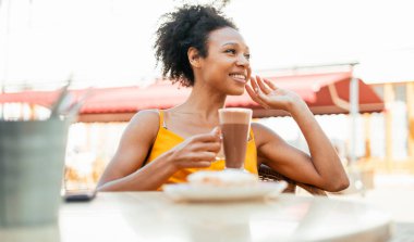  Kahvaltısını yapar, kakao içer ve kahvaltı yapar. Afro-Amerikan görünümlü bir kadın bir yaz restoranında otururken gülümsüyor..