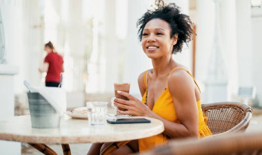 Serbest çalışan genç bir kız öğrenci yaz retoran 'ında kahvaltı yapıyor, gülümsüyor ve başka tarafa bakıyor.