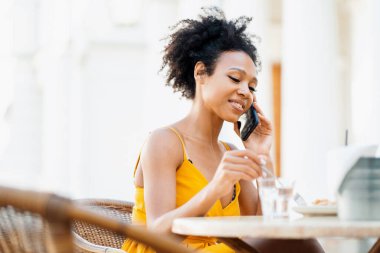Menajer çevrimiçi iş yapıyor. Serbest Afro etnik görünüm, bir yazlık kafede telefonla yapılan alışverişleri karşılıyor. Bir kadın blogcu müşterilerine sohbette cevap verir.